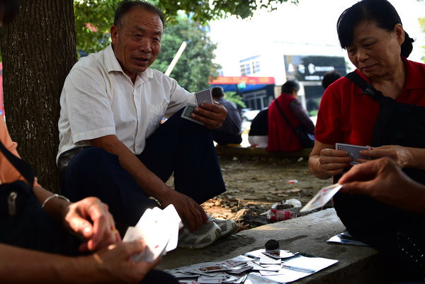 Kong Xianghai (izquierda), de 73 a?os, juega a las cartas mientras espera la salida del colegio de su nieto. después de jubilarse, Kong tiene dos ocupaciones principales: cuidar a su nieto y bailar en la plaza. [Foto: PPC]