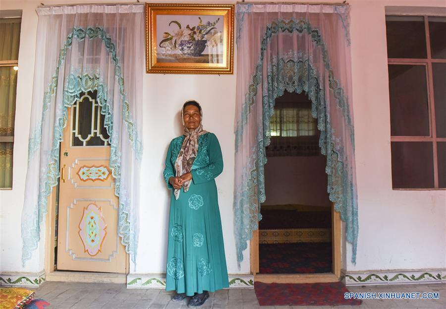 La foto tomada el primero de junio del a?o presente muestra a una mujer uygur en pie en el portal de su casa recién construida en la aldea Cele del pueblo del mismo nombre ubicado en el borde sure?o del desierto Taklimakan en la región autónoma uygur de Xinjiang. El pueblo retrocedió hacia el sur tres veces a lo largo de los cien a?os últimos debido al avance del desierto. Durante los últimos decenas de a?os, árboles como granada, azufaifo y nogal se vienen plantando en el pueblo, medida con la que el ingreso per cápita anual de los granjeros aumentó desde apenas 1.000 yuanes (154 dólares）en el pasado hasta 5.732 yuanes (882 dólares) en la actualidad. (Xinhua/Shen Qiao)